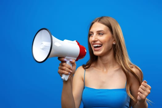 Young pretty woman with a megaphone against blue background in studio, close up