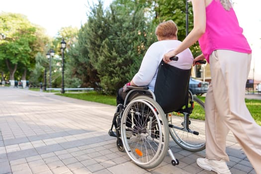 Young female caregiver pushing wheelchair with mature female person with disability across city street