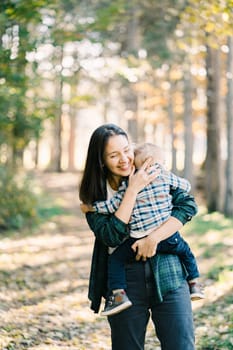 Smiling mother walks hugging a little girl in her arms through the forest. High quality photo