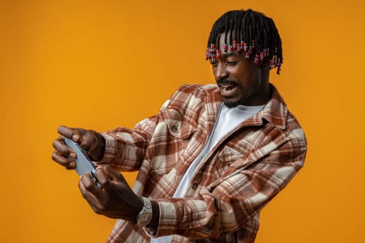 Young african man dressed in casual playing games on mobile phone over yellow background, close up