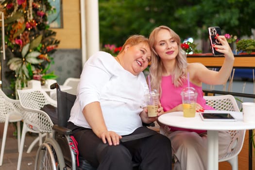 Portrait of mature mother in wheelchair and her daughter making a selfie using smart phone in cafe close up