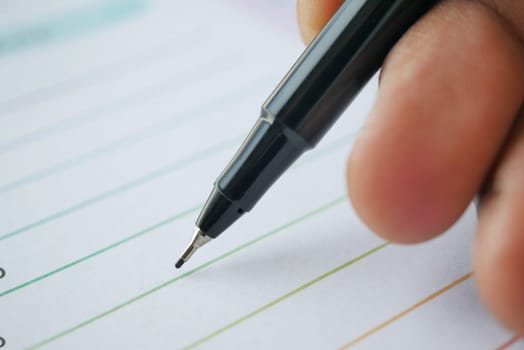 The hand of a man holding a pen on a piece of paper .