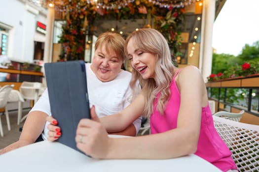 Mother with disability in wheelchair and her daughter using digital tablet while sitting at the table in cafe close up