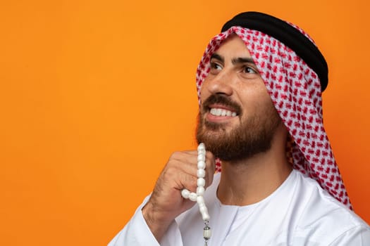 Young Arab man holding traditional beads against orange background close up