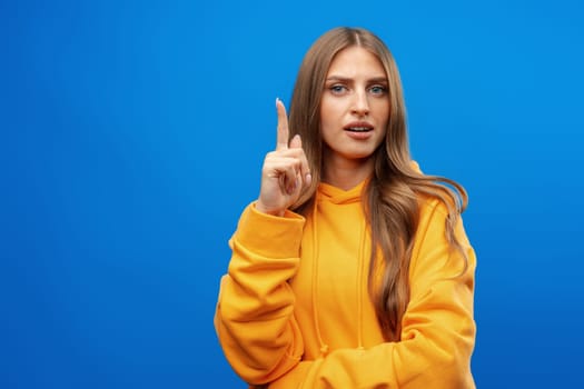 Smiling woman in hoodie posing in blue studio and pointing up