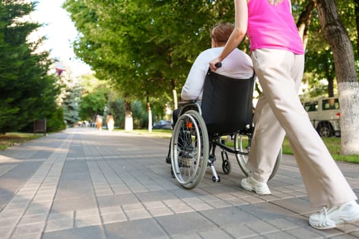 Young female caregiver pushing wheelchair with mature female person with disability across city street