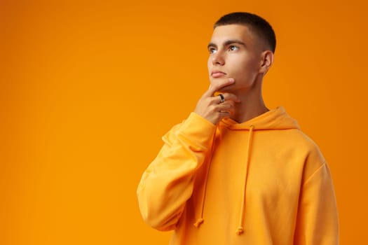 Pensive attractive young man thinking against yellow studio background close up