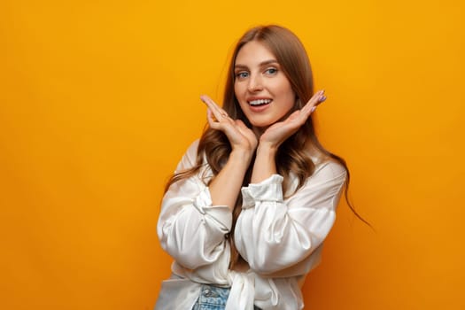 Young pretty surprised smiling woman standing with open palms on yellow background in studio