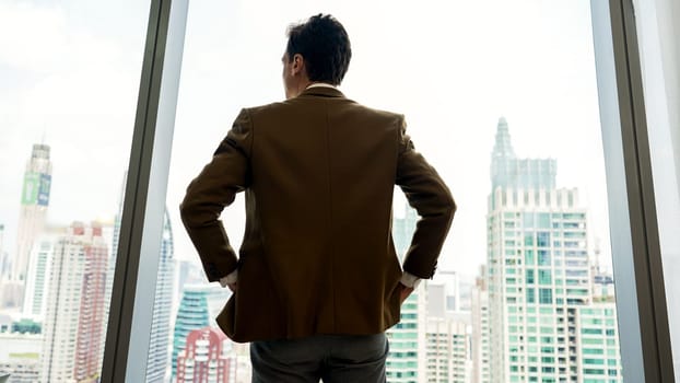 Back view ambitious businessman standing in ornamented office gazing out window to cityscape skyline. Determination and business ambition drive business career toward to bright future