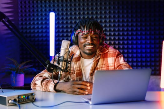 African radio host sitting at desk recording in studio with microphone and laptop close up