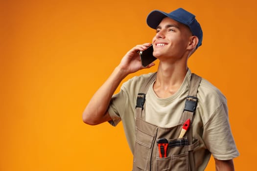 Young builder talking on a mobile phone against yellow background in studio