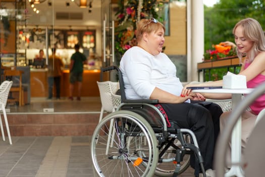 Woman with disability sitting in a wheelchair in outdoor cafe with her young daughter together