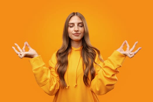 Young blonde woman making zen pose while meditating on yellow background close up