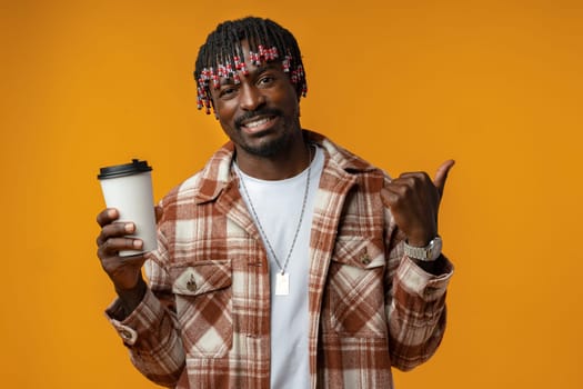 Young african man holding cup of take away coffee over yellow background close up