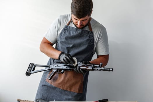 Close up of a man in apron wiping his firearm with a cloth in a workshop