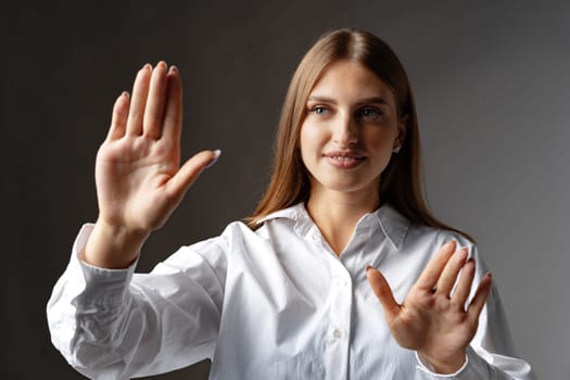 Young female entrepreneur touching virtual screen against grey studio background, close up