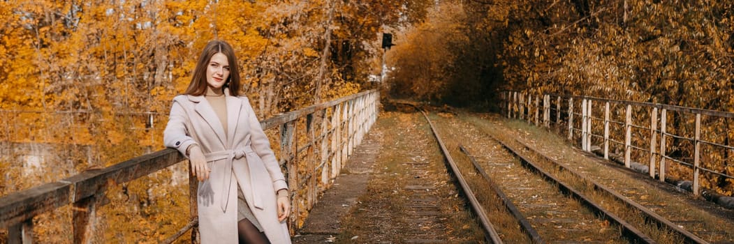 A beautiful long-haired woman walks through the autumn streets. Railway, autumn leaves, a woman in a light coat.