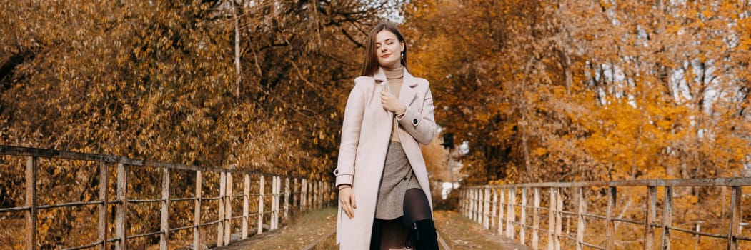 A beautiful long-haired woman walks through the autumn streets. Railway, autumn leaves, a woman in a light coat.