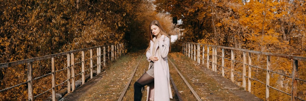 A beautiful long-haired woman walks through the autumn streets. Railway, autumn leaves, a woman in a light coat.