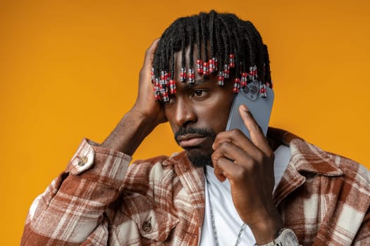 Young african man talking on smartphone stressed with hand on head on yellow background, close up