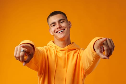 Handsome young man pointing hand at you on yellow background in studio