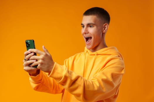 Portrait of a smiling young man holding mobile phone on yellow background, close up