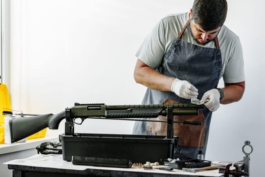 Close up of a man in apron wiping his firearm with a cloth in a workshop