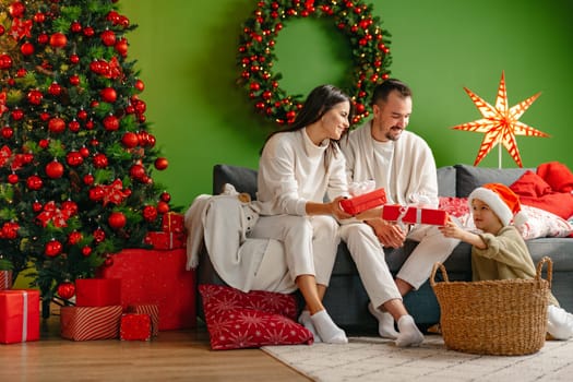 Happy young family sitting on sofa and relaxing at home at Christmas time