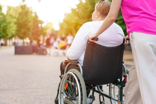 Back view of young woman helping mature woman in wheelchair strolling in the city