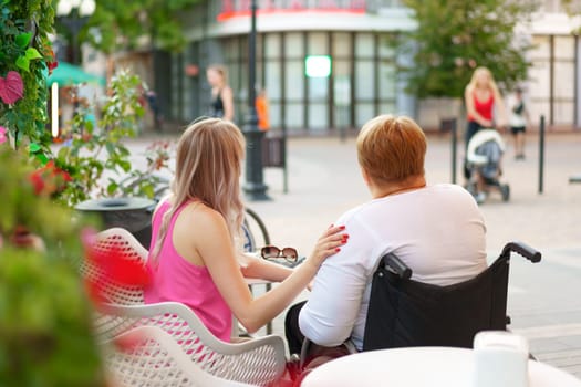 Woman with disability sitting in a wheelchair in outdoor cafe with her young daughter together