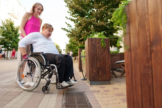 Young female caregiver pushing wheelchair with mature female person with disability across city street