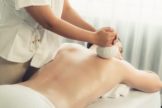 Hot herbal ball spa massage body treatment, masseur gently compresses herb bag on man body. Tranquil and serenity of aromatherapy recreation in day lighting ambient at spa salon. Quiescent