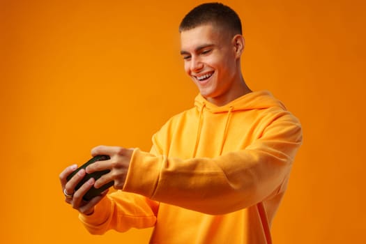 Portrait of excited young man playing online game on mobile phone on yellow background.in studio