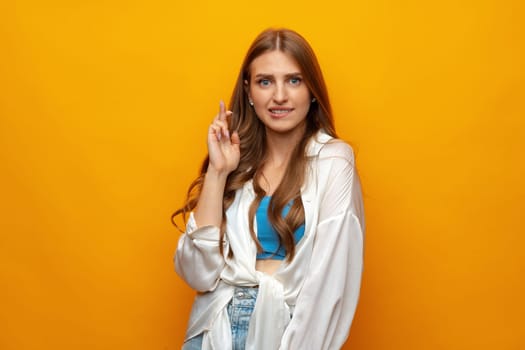 Young woman crossing her fingers and wishing for good luck on yellow background close up