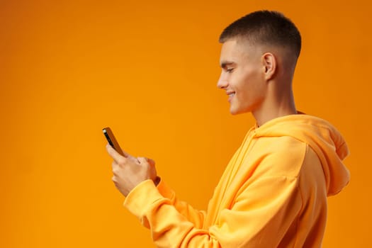 Portrait of a smiling young man holding mobile phone on yellow background, close up