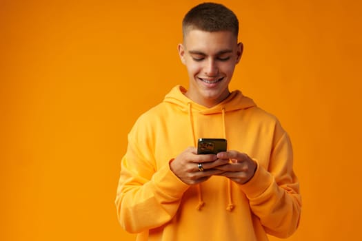 Portrait of a smiling young man holding mobile phone on yellow background, close up