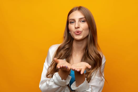 Portrait of cute lovely girl in casual outfit blowing kiss and looking at camera on yellow background, close up