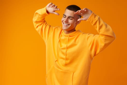 Handsome young man dancing near yellow wall close up