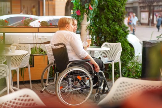 Woman with disability sitting in a wheelchair in outdoor cafe with her young daughter together