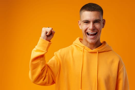 Portrait of a happy young man celebrating success against yellow background in studio