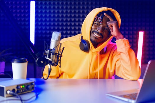 African radio host sitting at desk recording in studio with microphone and laptop close up