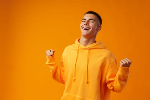 Portrait of a happy young man celebrating success against yellow background in studio