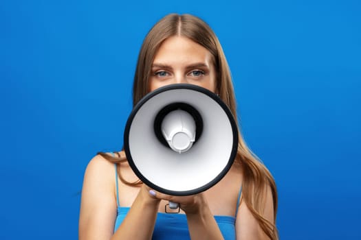 Young pretty woman with a megaphone against blue background in studio, close up