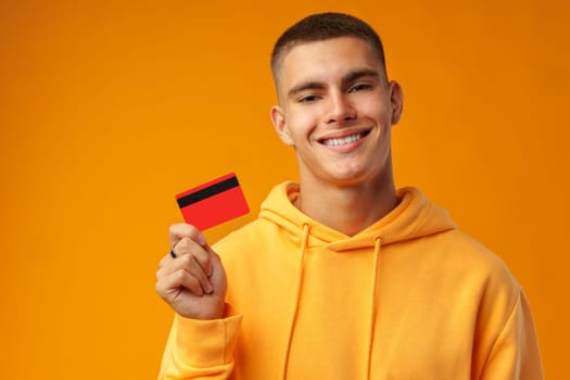 Handsome young man holding credit card on yellow color background in studio