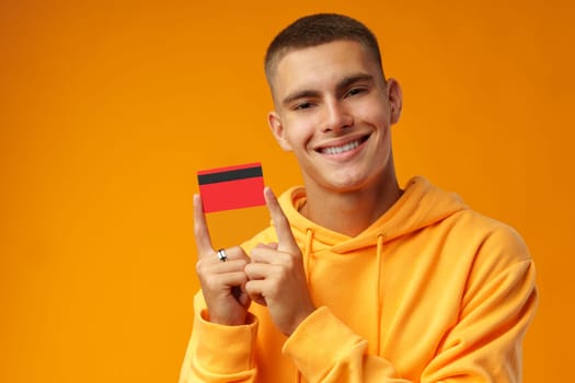 Handsome young man holding credit card on yellow color background in studio