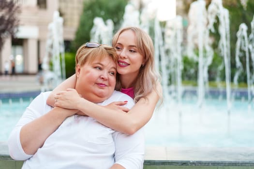 Positive young woman and her mother embracing on city street close up