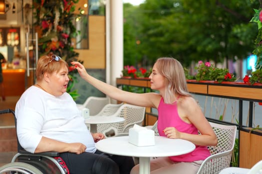 Woman with disability sitting in a wheelchair in outdoor cafe with her young daughter together