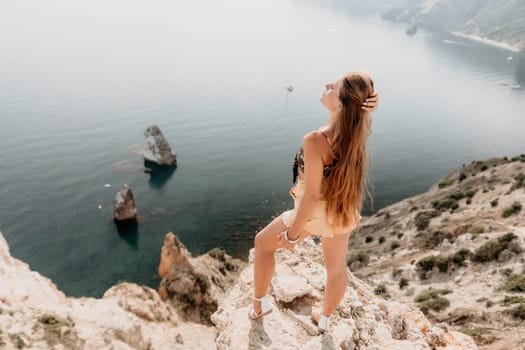 Woman travel sea. Happy tourist taking picture outdoors for memories. Woman traveler looks at the edge of the cliff on the sea bay of mountains, sharing travel adventure journey.