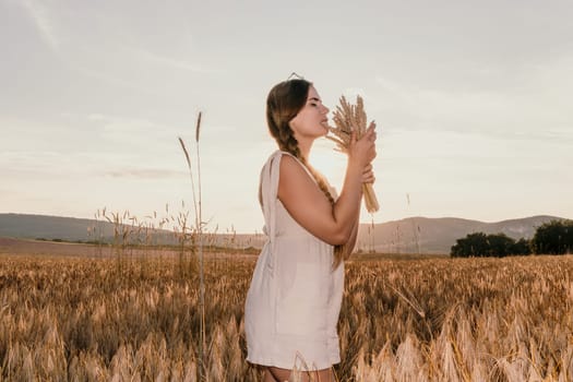 A woman is holding a bunch of wheat in her arms. The wheat is dry and brown, and the woman is wearing a white dress. The scene is set in a field, and the woman is posing for a photo