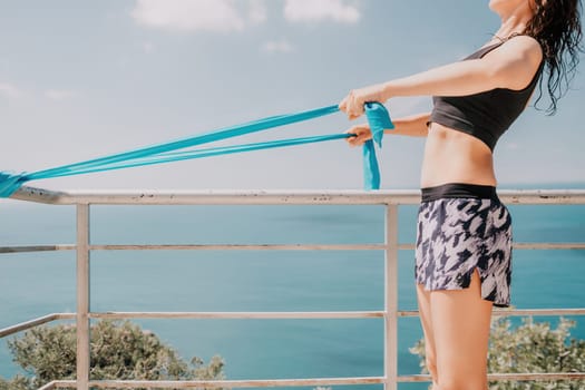 Middle aged well looking woman with black hair doing Pilates with the ring on the yoga mat near the sea on the pebble beach. Female fitness yoga concept. Healthy lifestyle, harmony and meditation.